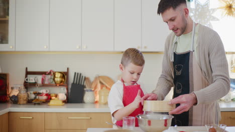 niño feliz ayuda a papá a tamizar la harina mientras trabaja en la cocina