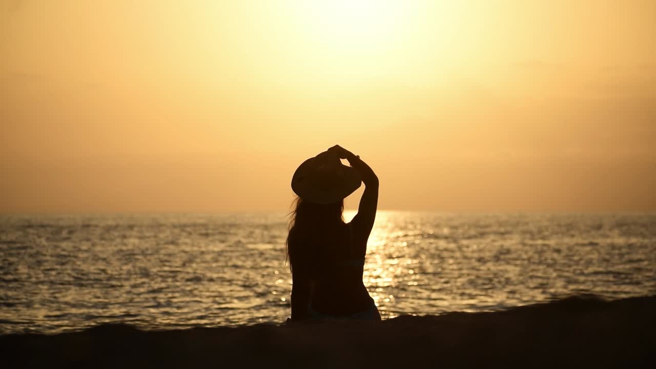 일몰 동안 해변에서 긴장을 풀고 휴식을 취하는 여성의 실루엣