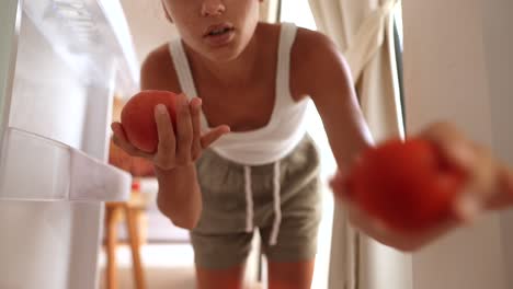 woman reaching into refrigerator for tomatoes