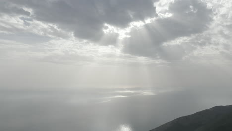 drone shot from the llogara view point near tirana in albania on a cloudy day in the shadows looking over the sea with god rays shining through the clouds onto the sea water log