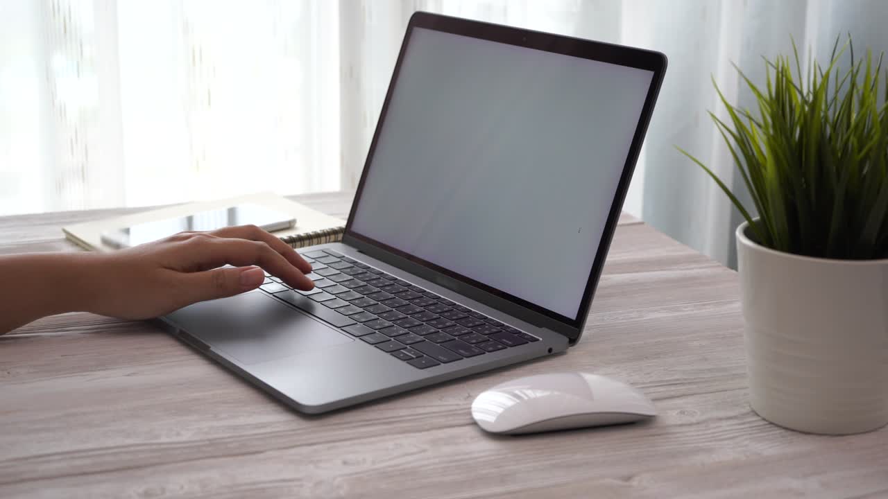 집에서 일하는 젊은 여성이 스마트폰과 노트북 컴퓨터를 테이블 위에 놓고, 여성의 손은 스마트폰 기술을 사용합니다.