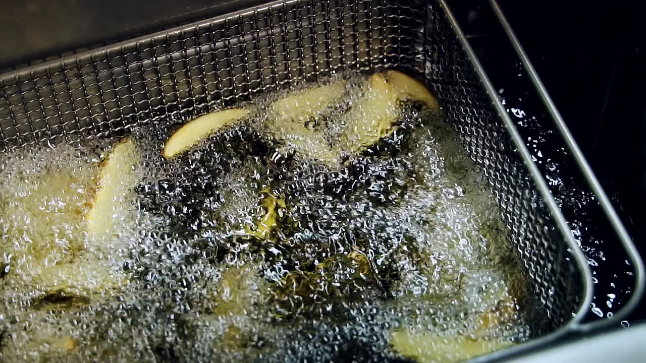 Cooking thin slices of french fries in boiling oil. Close-up. Slow motion