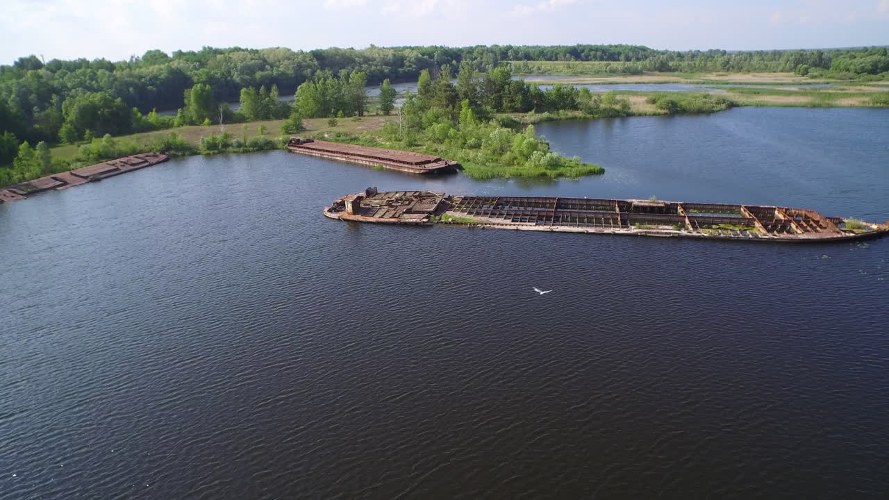Aerial view of decaying, rusted ships in Chernobyl's radioactive ship graveyard, Ukraine; nature reclaims industrial decay