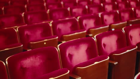 slow tracking movement over worn empty red velvet theatre audience chairs