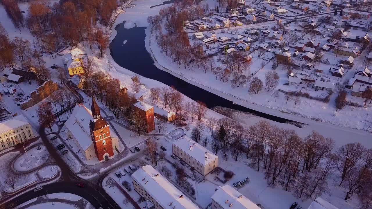 hermosa vista aérea sobre valmiera durante el invierno, mostrando casas nevadas, edificios, río gauja e iglesia bajo el cálido resplandor del sol de la tarde