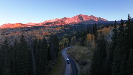 beautifully lit mountain peaks, fall foliage and an airstream and jeep rolling down the road during sunrise