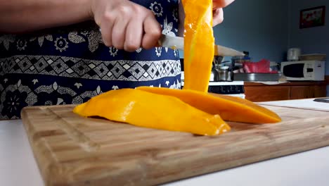 mujer usa un cuchillo para cortar un mango fresco grande, quitando el hoyo