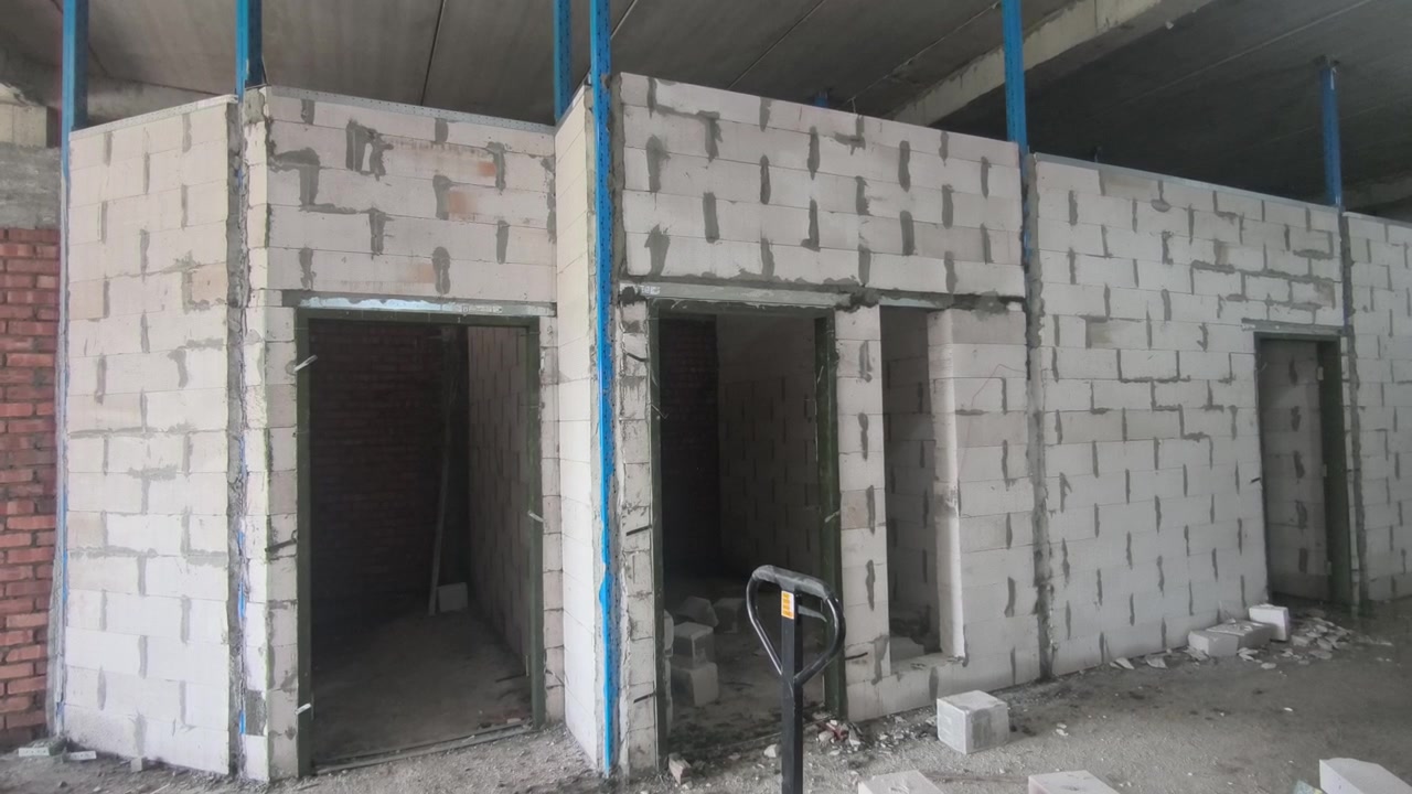 Montaż ściany z bloczków betonu komórkowego (AAC) na placu budowy. Zawiera metalowe usztywnienia i nadproża dla efektywności konstrukcyjnej. Nowoczesne techniki murarskie przyspieszają postęp budowy.