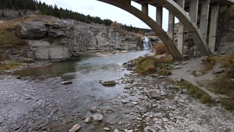 slo-mo aerial shot approaching lundbreck falls while flying underneath an arch bridge in southern alberta, canada