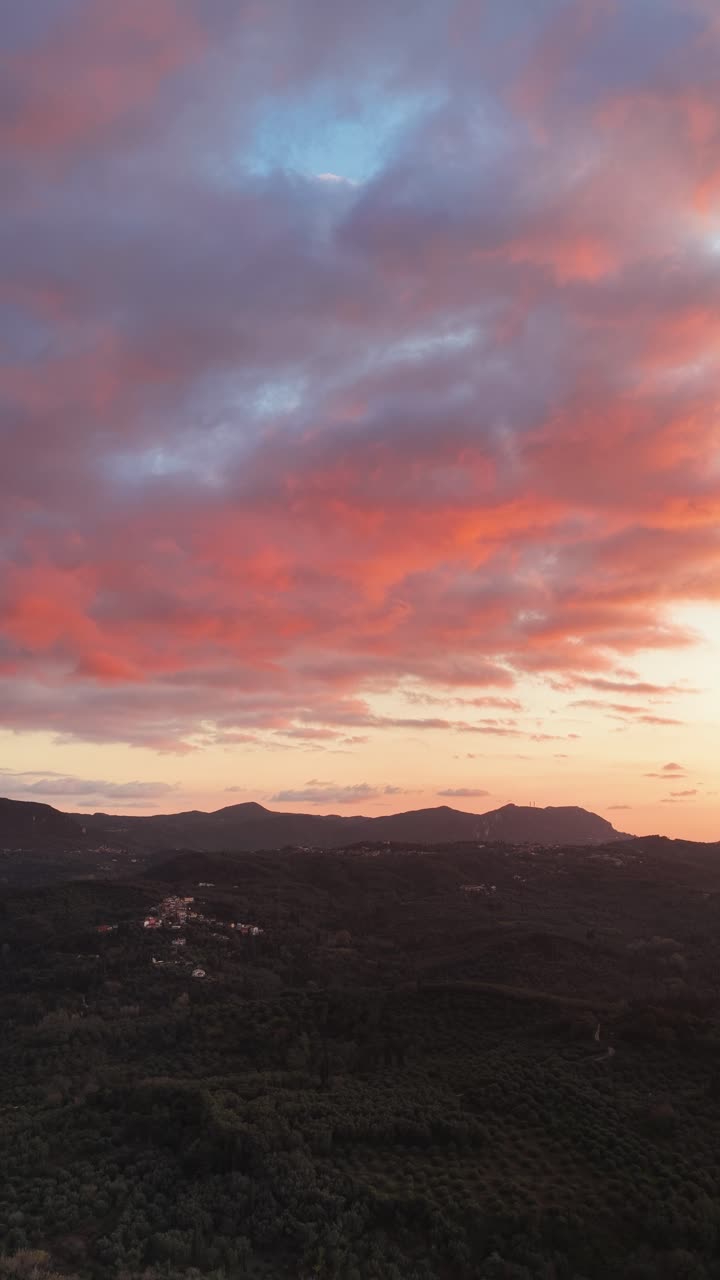 Aerial Vertical View of Dramatic Pink and Orange Sunset Clouds Over Dark Rolling Hills in Corfu Greece