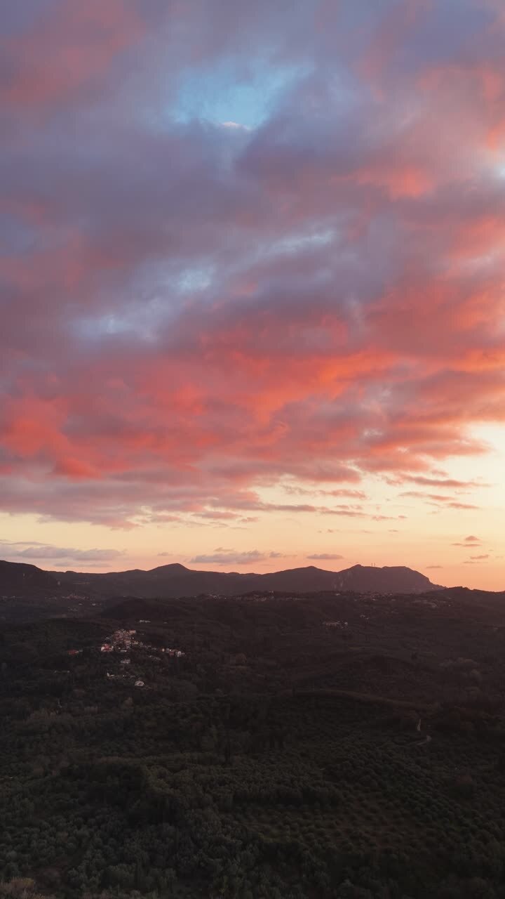 Aerial Vertical View of Dramatic Pink and Orange Sunset Clouds Over Dark Rolling Hills in Corfu Greece