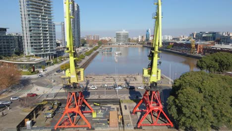 aerial view of a waterway flying between two cranes over a bridge at buenos aires city