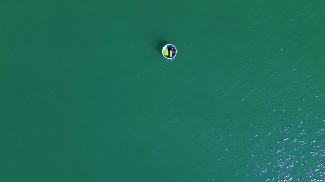 Drone captures a bird’s-eye view of crystal-clear turquoise waters with a bucket boat gliding smoothly, carrying people enjoying the sea.