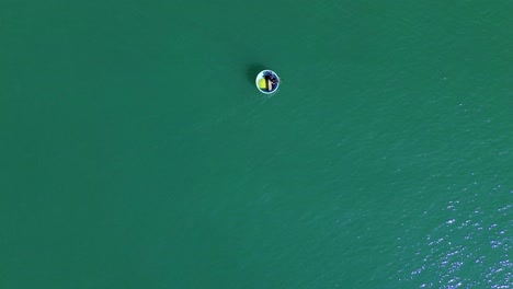 drone captures a bird’s-eye view of crystal-clear turquoise waters with a bucket boat gliding smoothly, carrying people enjoying the sea.