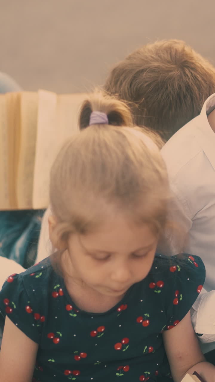 young blond lady in black dress with red cherry images talks to brothers sitting on pavement at asphalt road closeup