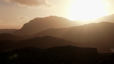 a slow left panning shot of an intense golden sunset bathing a silhouetted mountainous landscapes in evening light in the highlands of scotland