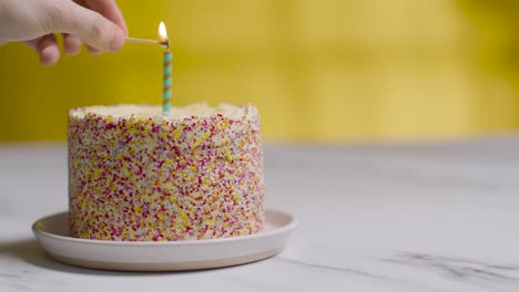 Single-Candle-Being-Lit-By-Hand-On-Studio-Shot-Of-Birthday-Cake-Covered-With-Decorations-3