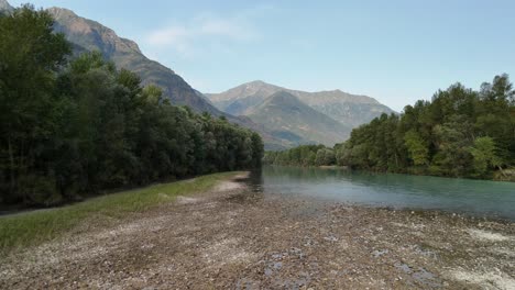 a tranquil, slow pan revealing the serene toce river winding through dense forests, with majestic mountains towering in the background at ansola italy
