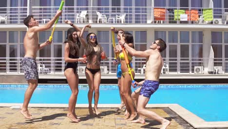 Felices-Jóvenes-Amigos-Alegres-Bailando-Y-Divirtiéndose-En-La-Piscina.-Fiesta-En-La-Piscina-De-Verano-Con-Pistolas-De-Agua.-Tiro-En-Cámara-Lenta