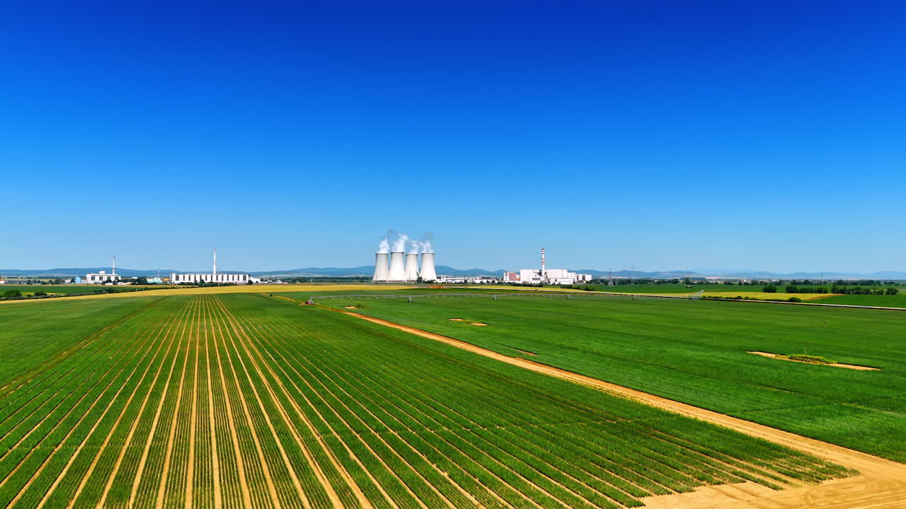 Green plantations with drip irrigation system. Wide pipes of the plant at backdrop produce white smoke. Slovakia