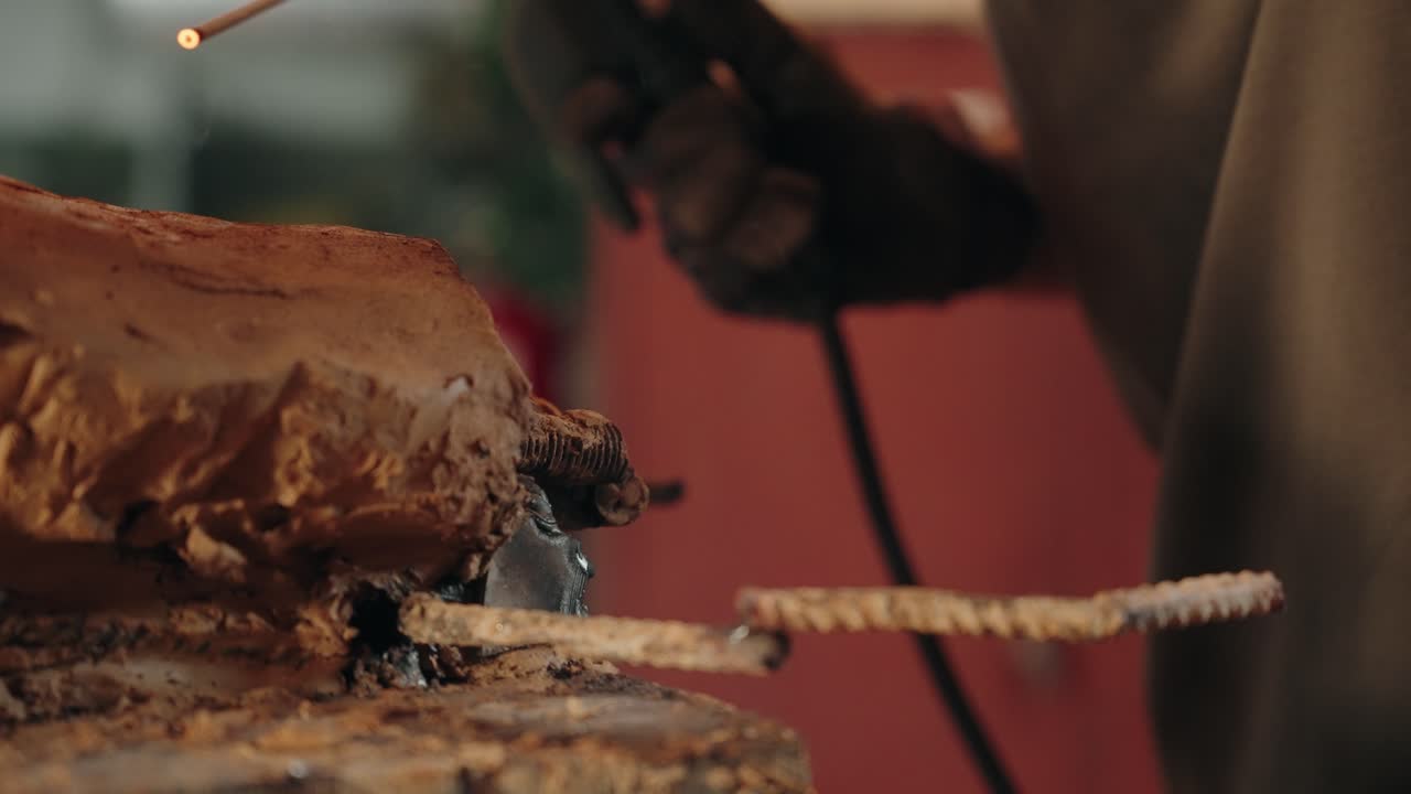 Welding rebar frame into clay sculpture in artisan workshop with sparks