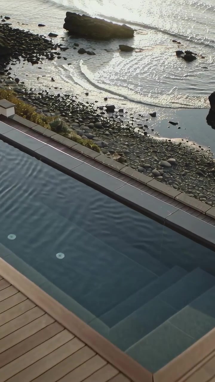 Vertical video: Panning camera starting high, revealing infinity pool on coastal deck, ocean beyond