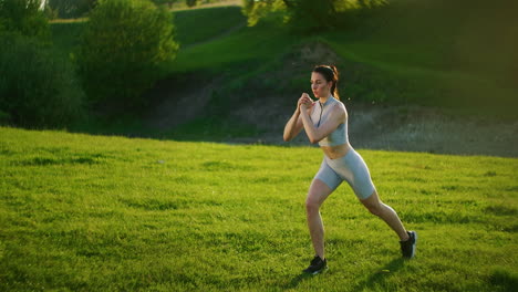 A-woman-makes-lunges-during-a-training-session-in-the-park-and-raises-her-leg-in-the-knee