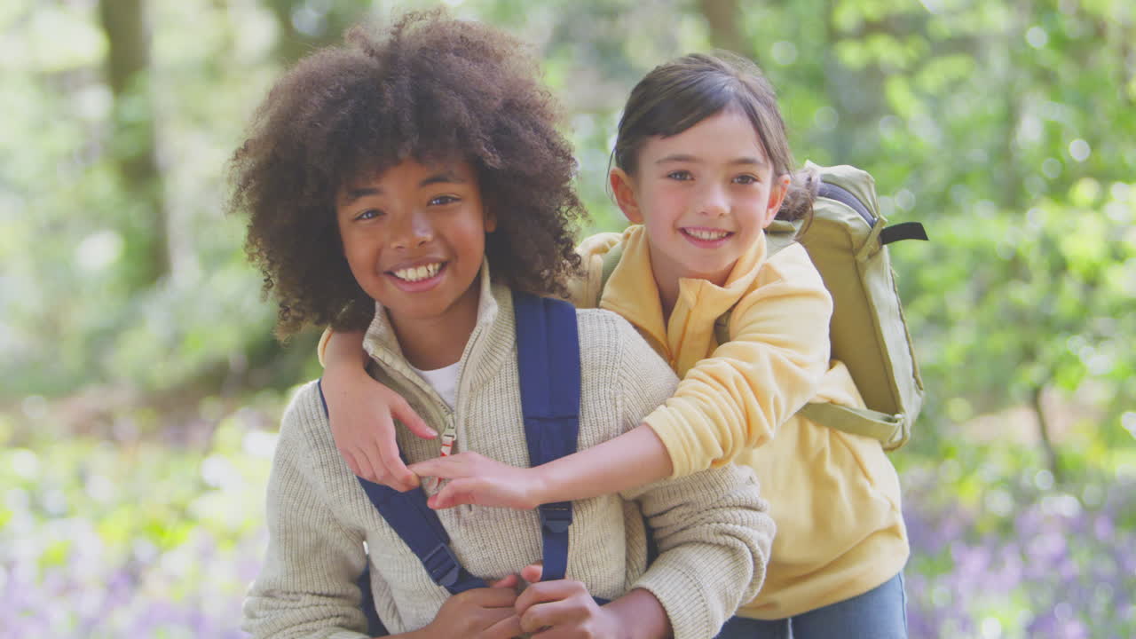 retrato de un niño y una niña con mochilas caminando por los bosques de bluebell en primavera