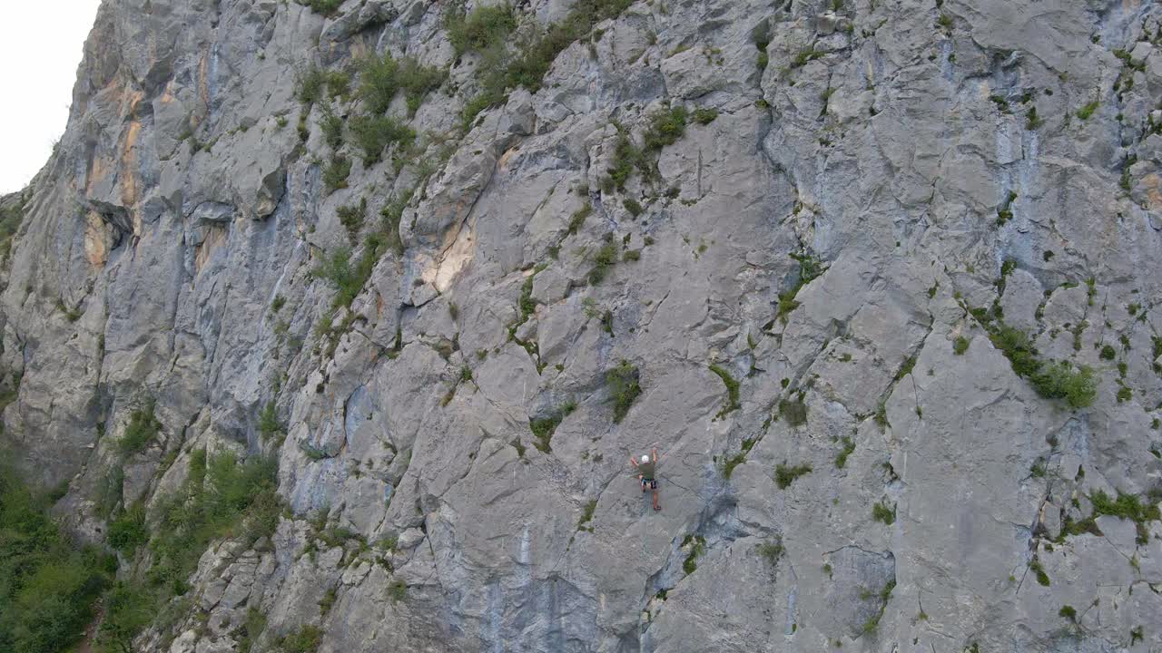 Distant static drone footage of a man stopped while lead climbing in the Pyrenees moutains at Tarascon sur Ari&egrave;ge