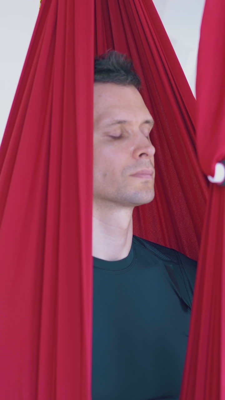 concentrated handsome man sits relaxed and meditates in modern red anti-gravity yoga hammock close view