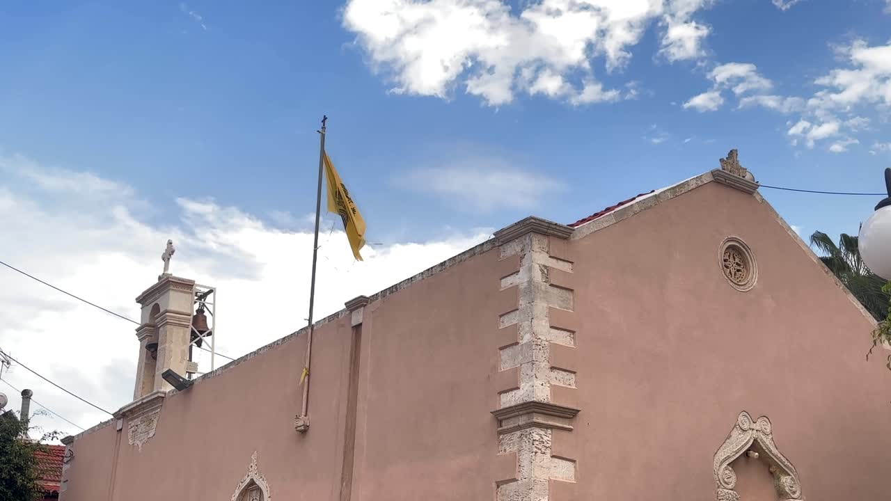 Chiesa storica con mura beige e bandiera greca a Hersonissos, Creta, Grecia.