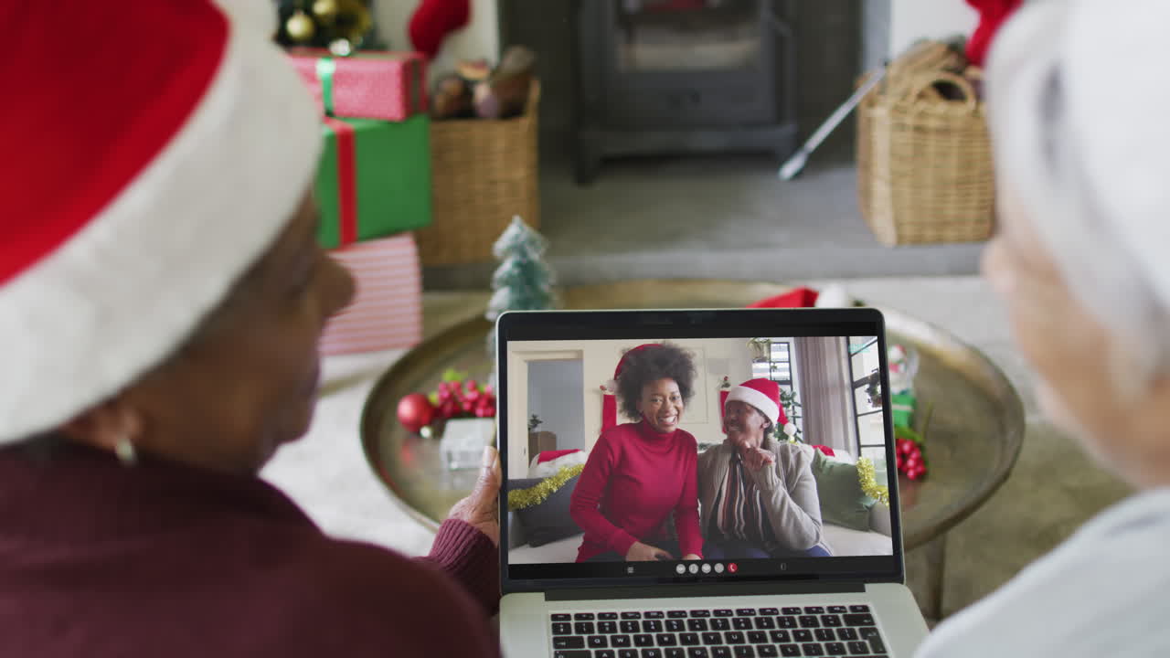 amigas mayores diversas usando una computadora portátil para una videollamada de navidad con una familia sonriente en la pantalla