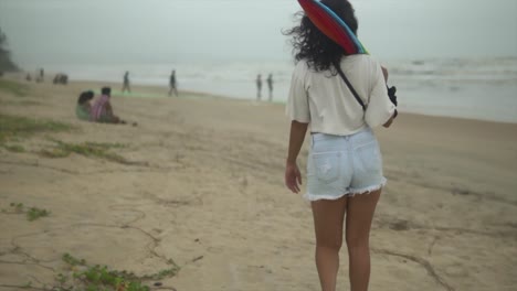 Young-Brunette-girl-with-a-colored-umbrella-walking-slowly-along-the-shore-of-a-beach