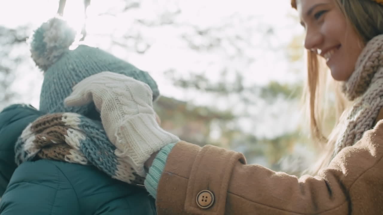 공원에서 겨울 옷을 입은 어머니와 아기, 어머니는 모직 모자를 쓰고 그녀를 안아줍니다.