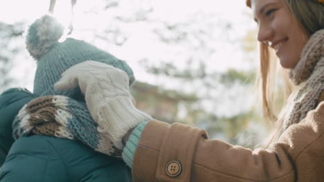 madre y su bebé con ropa de invierno en el parque, la madre se pone el sombrero de lana y la abraza