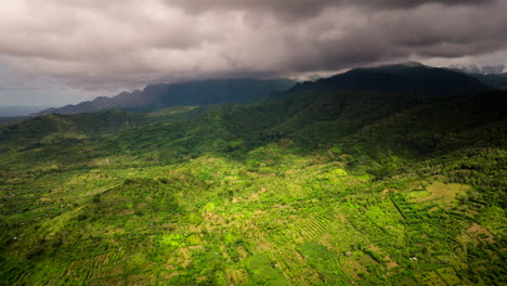 Retroceso-Aéreo-Sobre-La-Luz-Del-Sol-En-Un-Campo-De-Arroz-En-Terrazas-Verdes-Mientras-La-Nube-De-Tormenta-Pasa-Por-La-Montaña