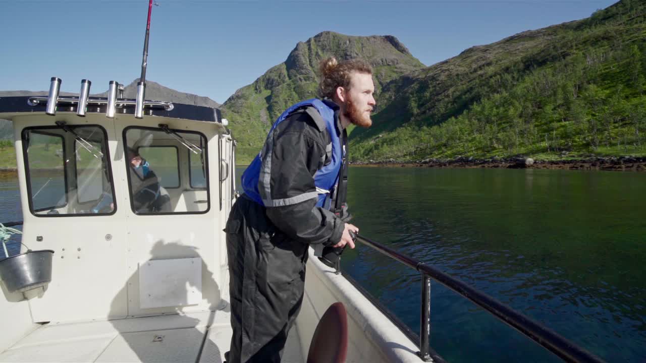 Rejsende med kamera på en sejlbåd med frodige bjerge i baggrunden på en solrig dag i Norge. - Mellembillede