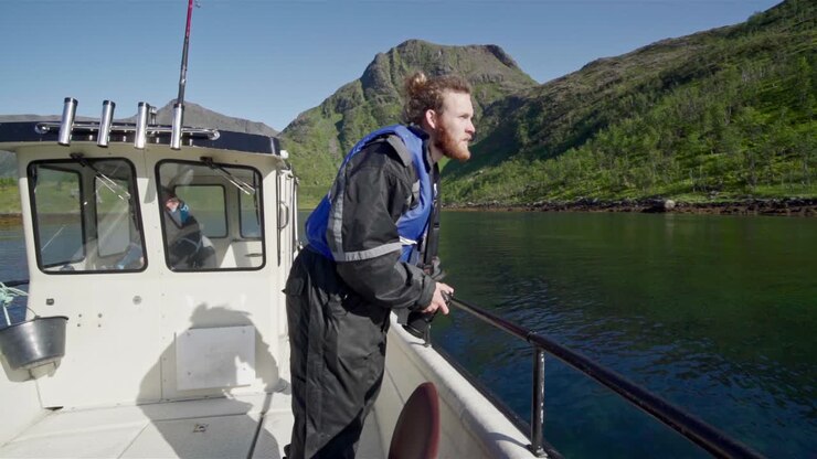 Viaggiatore con macchina fotografica su una barca a vela con montagne lussureggianti sullo sfondo durante una giornata di sole in Norvegia. - Inquadratura media