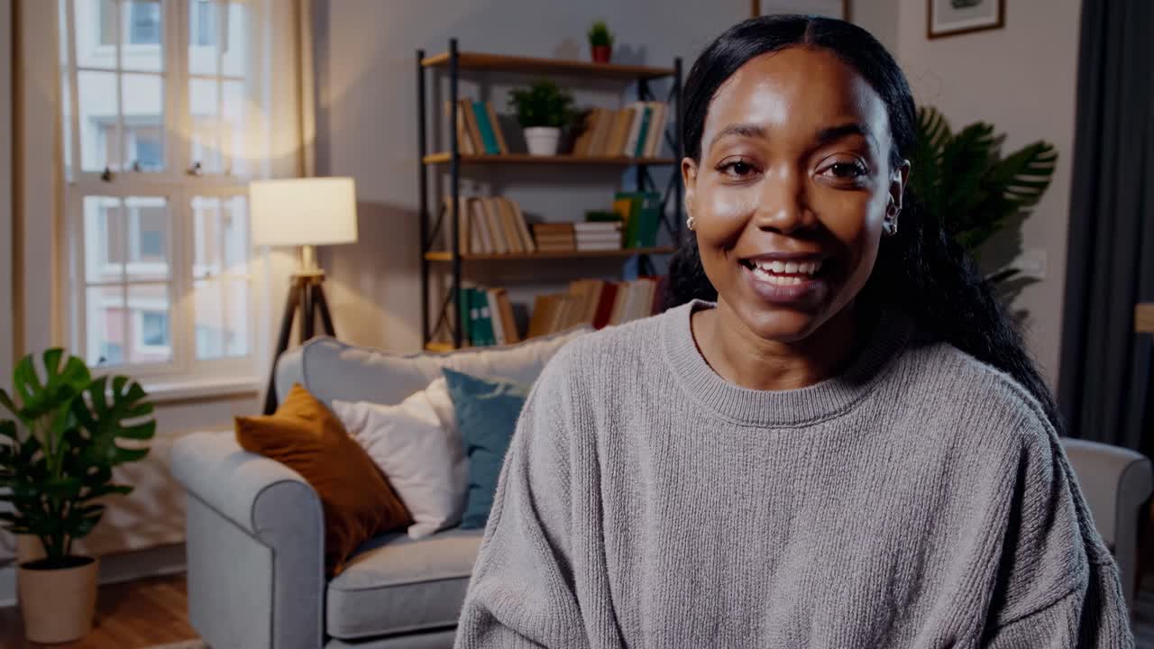 A woman in a cozy living room setting speaks directly to the camera in a medium close-up angle