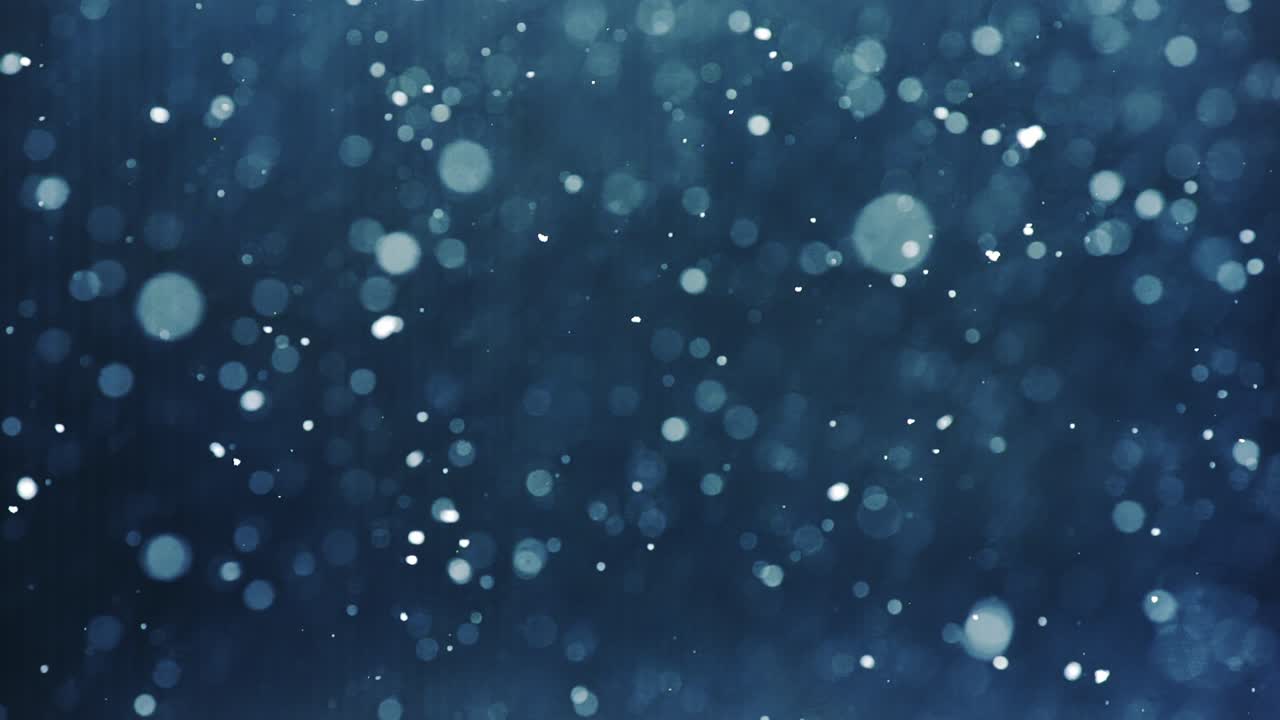Gentle snowflakes dance in slow motion on dark blue background with bokeh