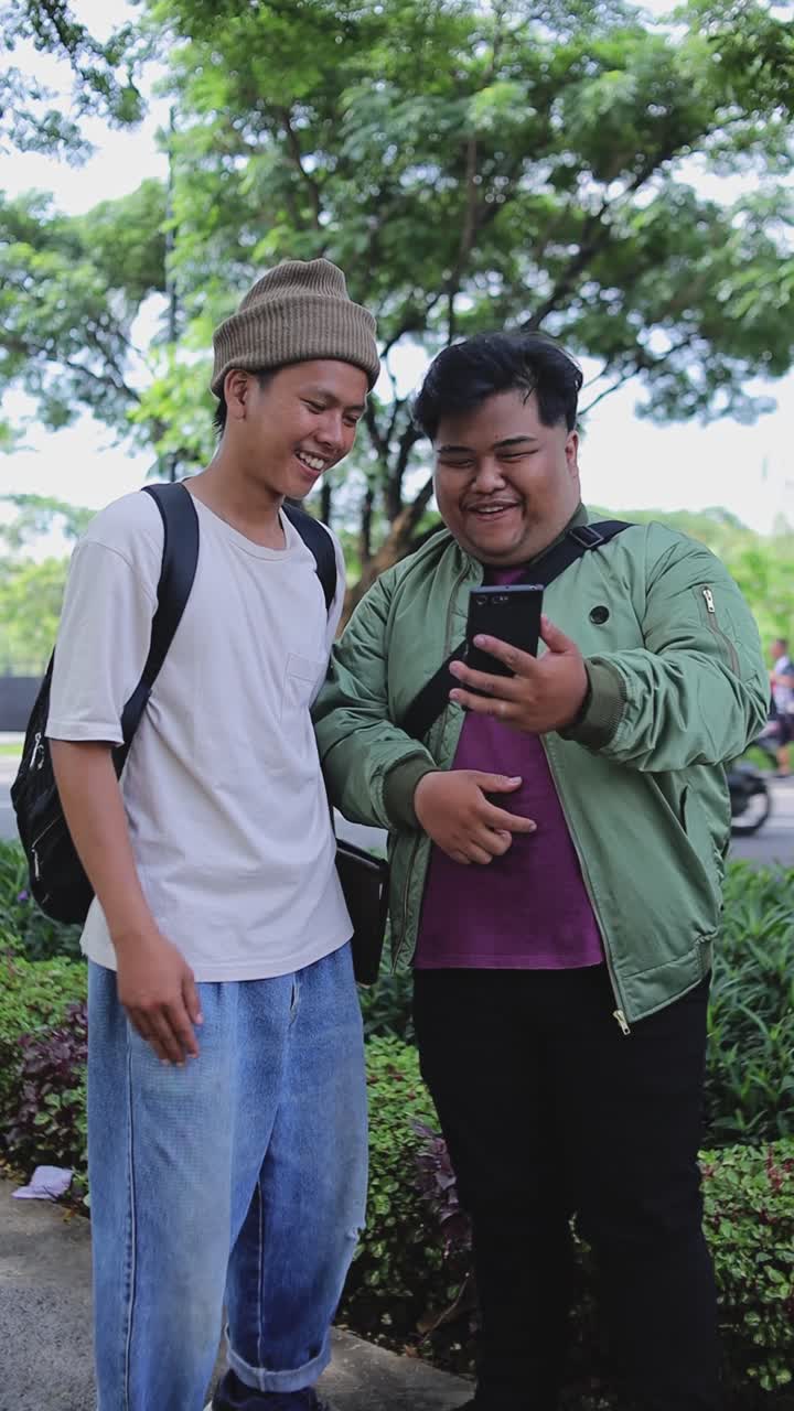 Video Vertikal Dua Mahasiswa Asia Pria Menggunakan Ponsel Bersama Sambil Berdiri Di Taman