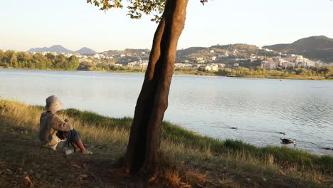 Frau-Sitzt-Am-See,-Schwimmende-Enten,-Seeblick