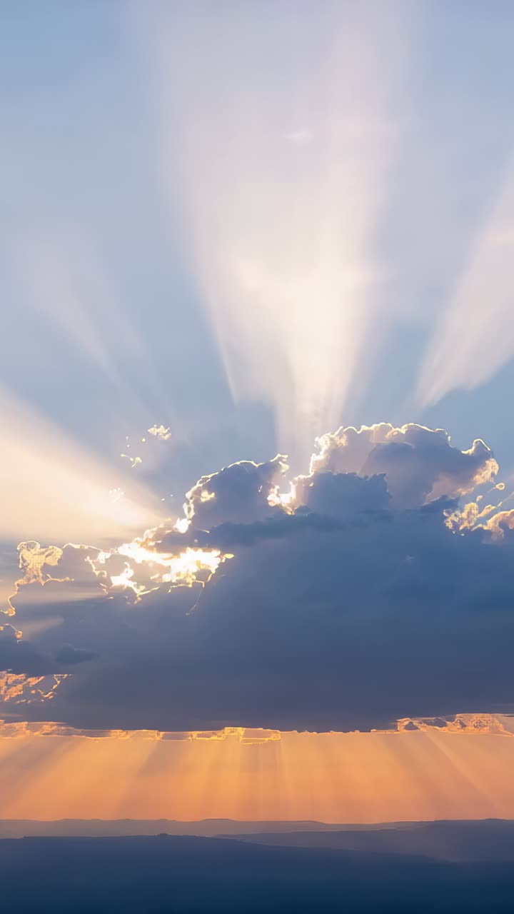 Vertical video: Moving sun behind dark cumulus cloud casting light shafts at sunset, orange horizon
