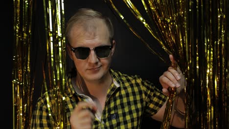 Portrait-of-caucasian-man-posing-on-black-background.-Gold-shining-foil-strips.-Party,-music,-disco