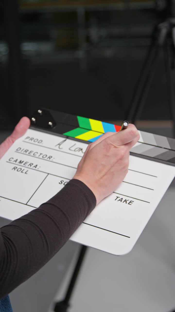 vídeo vertical de la asistente femenina en el set de la película en el estudio escribiendo detalles de la producción de la película o el video en clapperboard o pizarra
