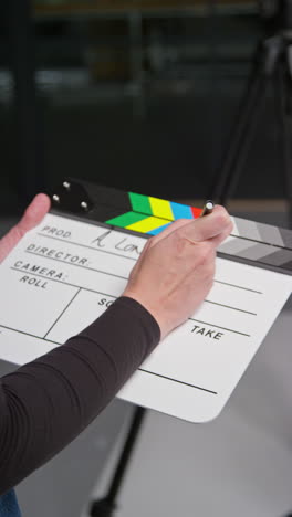 vertical video of female assistant on film set in studio writing movie or video production details down on clapperboard or slate