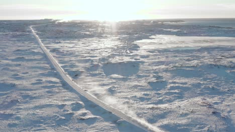 long snowy road in middle of arctic landscape of iceland with bright sunlight