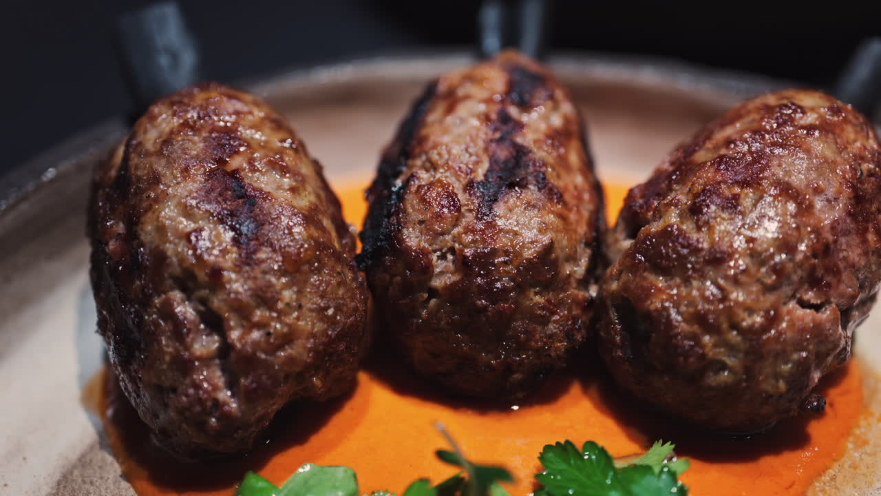 Three grilled meat skewers on charcoal sticks served on a plate with an orange sauce