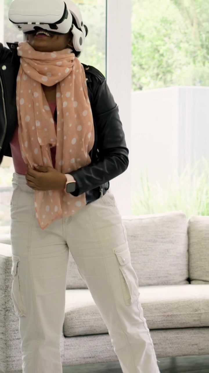 Vertical video: Following prompts woman with peach scarf pacing home sofa, adjusting VR headset