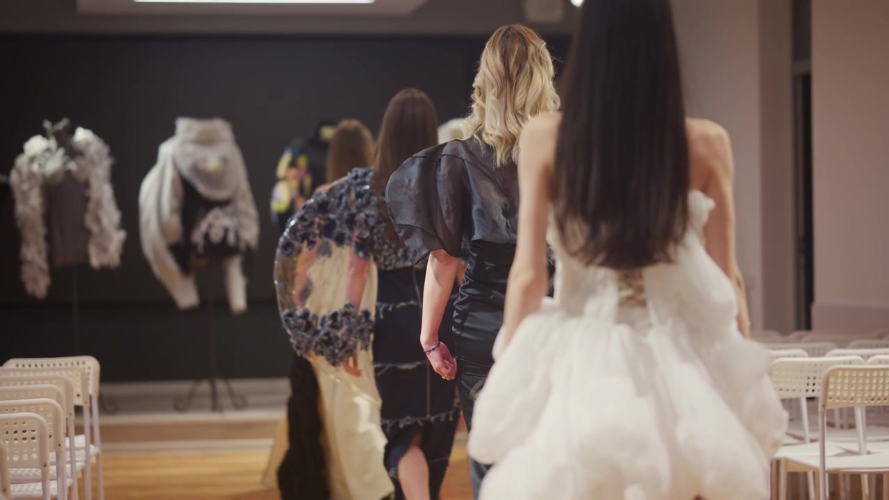 Modeller set bagfra iført forskellige kjoler går ned ad en catwalk med tomme stole.